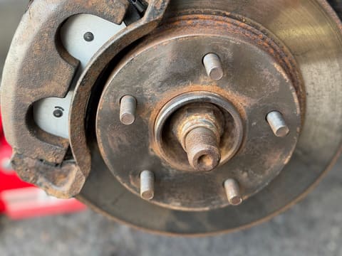 Rusty caliper and rotor with bright new brake pads showing through the caliper windows