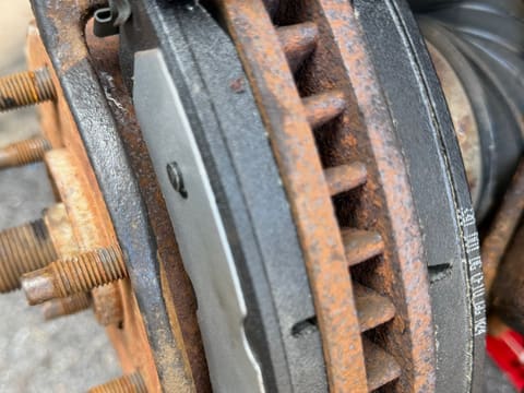 Close-up of heavy orange rust between the cooling vanes of a vented brake rotor, beside the caliper bracket