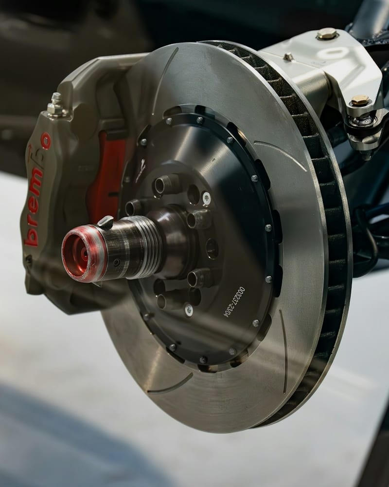 Drilled brake rotor and red performance caliper on a car supported by jack stands